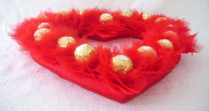 Tulle is a bright material, it can easily help decorate a gift. Cut out the base-heart from the foam, glue it over with corrugated paper and braid. Glue a row of sweets decorated with tulle on top