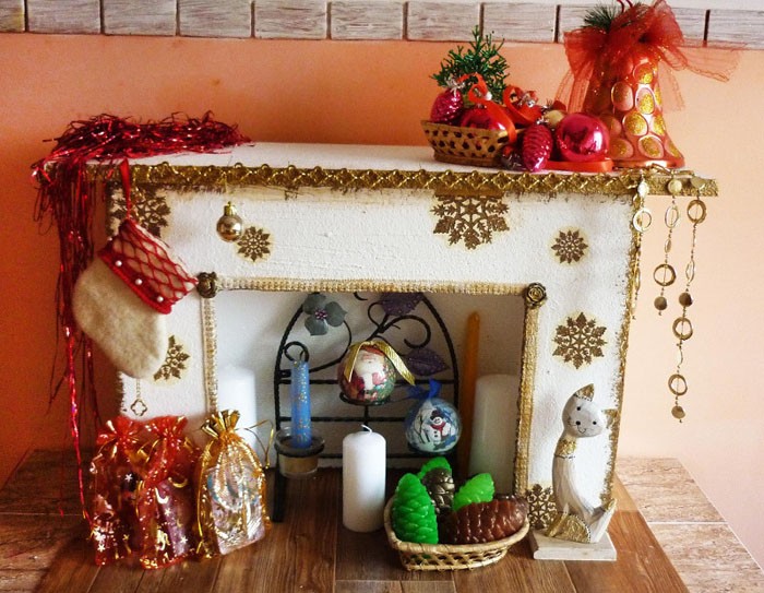 Hình nón và đồ trang trí cây thông Noel, hạt được kết hợp với một lò sưởi như vậy. Trang trí có thể được đặt trên nắp của sản phẩm hoặc treo từ các vết cắt bên trên đinh tán văn phòng phẩm